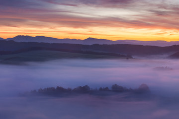 Sunset Over Misty Landscape Scenic View Of Foggy Morning Sky With Rising Sun Above dreamy Forest. Mountain range with visible silhouettes through the morning colorful fog  Beautiful background concept