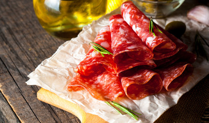 Italian salami with olives and spices on wooden background