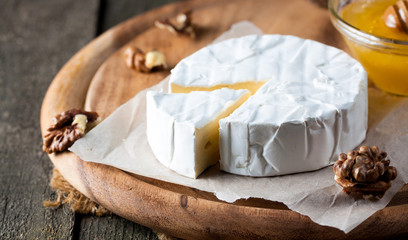 Brie type of cheese. Camembert cheese. Fresh Brie cheese and a slice on a wooden board with nuts, honey and leaves. Italian, French cheese.
