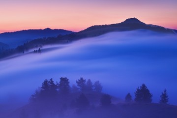 Sunset Over Misty Landscape Scenic View Of Foggy Morning Sky With Rising Sun Above dreamy Forest. Mountain range with visible silhouettes through the morning colorful fog  Beautiful background concept