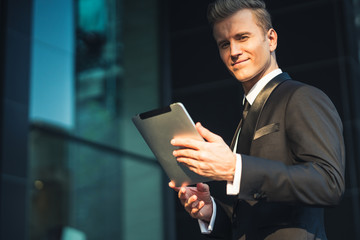 leader handsome caucasian businessman standing and work with tablet in black suit office building entance