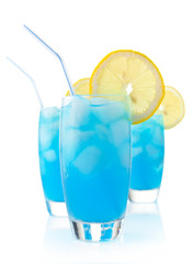 Blue lagoon cocktails with ice cubes, lemon and straw on white