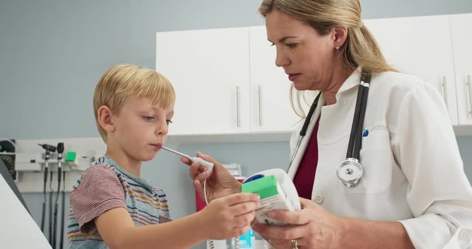 Friendly female pediatrician using digital thermometer to check temperature of sick little boy. Child patient with a fever visiting doctor. Slow motion 4k