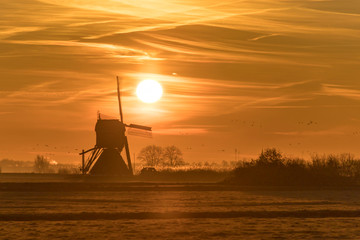Sunrise over a historic Dutch windmill on a foggy horizon in the countryside 