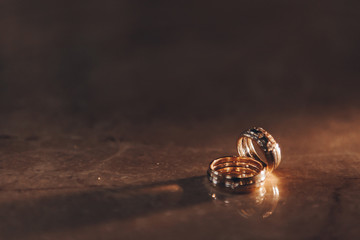 Gold rings on a dark background, under the beam of light with reflection in the glass