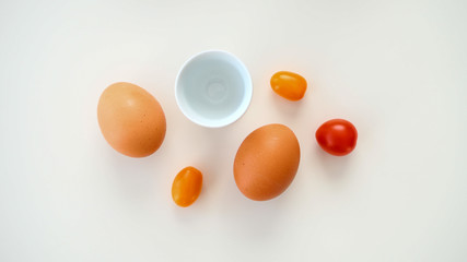 Jajka na miękko z podstawką oraz leżące pomidorki koktajlowe na białym tle - obrazy, fototapety, plakaty