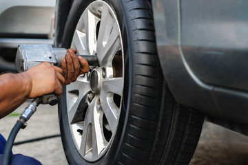 Tire Replacement concept. Mechanic Using Electric Screwdriver Wrench for Wheel Nuts in Garage. Car...