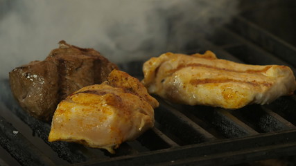 beef and two pieces of chicken fillet or turkey on the grill brought to the ready in the background a flame of coals and smoke