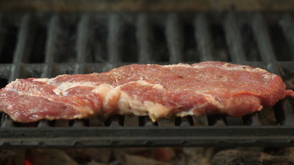 Beef steak, pork or veal marinated with spices and beaten with a hammer lies on the grill, in the background smoke from coals, the background is washed, the view of the video with the side close-up
