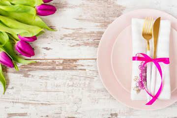 Easter table setting, flatlay ? wedding party, event decoration. Pink dishes and a gold fork and a spoon on a light rustic wooden background. Beautiful purple spring tulip flowers
