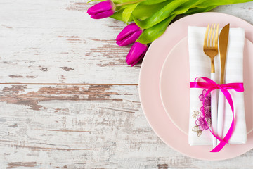 Easter table setting, flatlay ? wedding party, event decoration. Pink dishes and a gold fork and a spoon on a light rustic wooden background. Beautiful purple spring tulip flowers