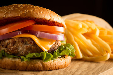 Home made hamburger with beef, onion, tomato, lettuce and cheese. Fresh burger close up on wooden rustic table with potato fries, beer and chips. Cheeseburger.