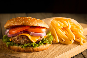 Home made hamburger with beef, onion, tomato, lettuce and cheese. Fresh burger close up on wooden rustic table with potato fries, beer and chips. Cheeseburger.