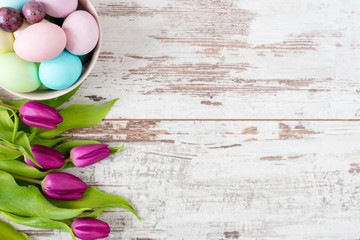 Easter eggs Pastel colored. Beautiful spring flowers - purple tulips on a light rustic wooden background. Floral frame with stunning flowers. Copy space