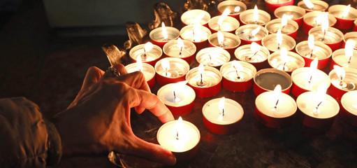 hand of an old widow who prays with the lighted candles in the p