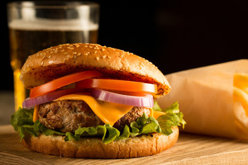 Home made hamburger with beef, onion, tomato, lettuce and cheese. Fresh burger close up on wooden rustic table with potato fries, beer and chips. Cheeseburger.