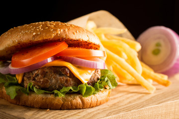 Home made hamburger with beef, onion, tomato, lettuce and cheese. Fresh burger close up on wooden rustic table with potato fries, beer and chips. Cheeseburger.