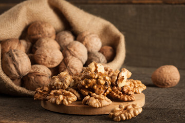 Walnut kernels in sack and whole walnuts on rustic old wood.