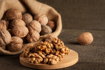 Walnut kernels in sack and whole walnuts on rustic old wood.