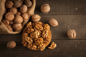 Walnut kernels in sack and whole walnuts on rustic old wood.