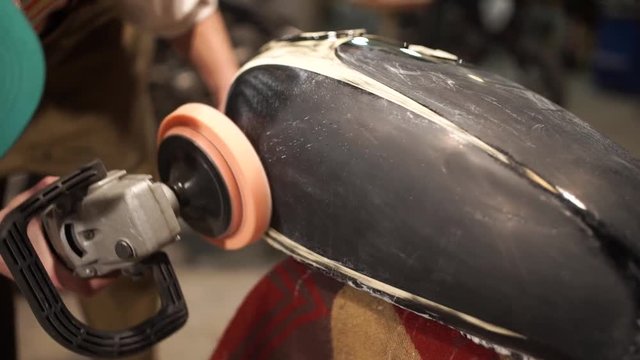 Guy polishing metal gas tank. Auto mechanic assembles custom motorcycle in his workshop. Guy create an exclusive motobike cafe racer in the garage.