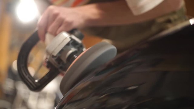 Guy polishing metal gas tank with sandpaper. Auto mechanic assembles custom motorcycle in his workshop. Guy create an exclusive motobike cafe racer in the garage.