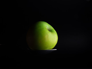 green apple on a spoon, dark background