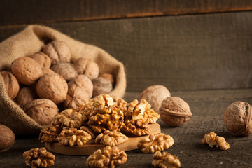 Walnut kernels in sack and whole walnuts on rustic old wood.