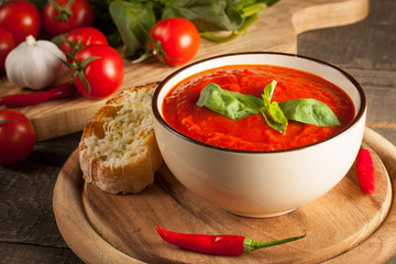 Fresh, healthy tomato soup with basil, pepper, garlic, tomatoes and bread on wooden background. Spanish gazpacho soup.