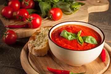 Fresh, healthy tomato soup with basil, pepper, garlic, tomatoes and bread on wooden background. Spanish gazpacho soup.
