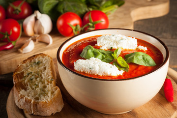 Fresh, healthy tomato soup with basil, pepper, garlic, tomatoes and bread on wooden background. Spanish gazpacho soup.