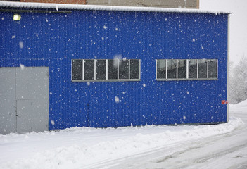 Snowfall on the background of an industrial warehouse of blue metal.