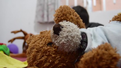 teddy bear left alone while two years old boy is playing with other toys in the background
