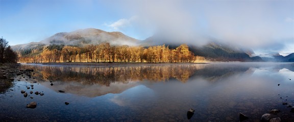 Fototapeta premium Scottish Loch in the early morning. A very calm autumn day at Loch Voil, near Balquhidder in the Loch Lomond and Trossachs National Park, Scotland. Beautiful landscape reflection in water.