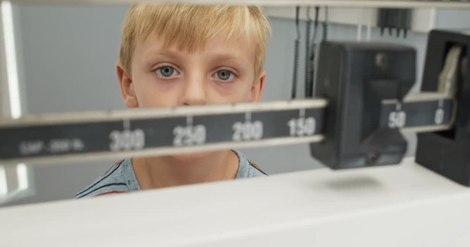 Close up of little boy being weighed on scale at doctors office. Child patient visiting pediatrician for regular check up. Slow motion 4k