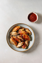 BBQ spicy chicken wings served in ceramic plate with red sauce over white marble background. Flat lay, space.