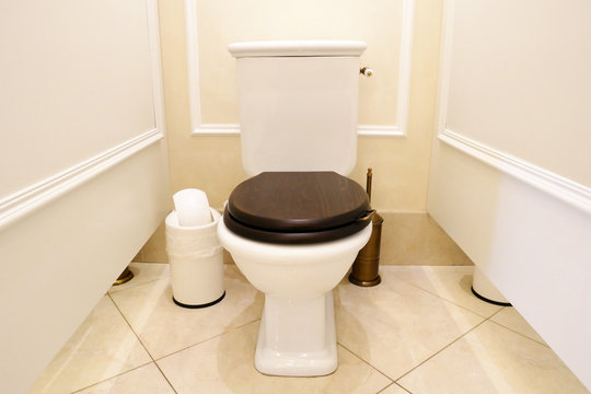 White toilet with wooden lid in the toilet, public toilet stall.