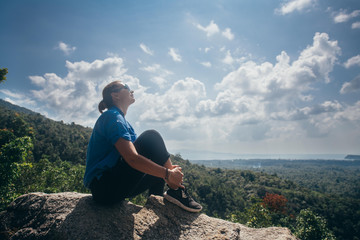 Naklejka premium A young woman is sitting on a stone on top of a mountain.