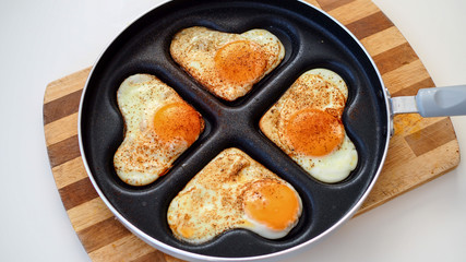 Jajka sadzone w kształcie serc na patelni leżące na drewnianej desce na białym tle