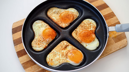 Jajka sadzone w kształcie serc na patelni leżące na drewnianej desce na białym tle