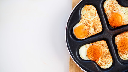 Jajka sadzone w kształcie serc na patelni leżące na drewnianej desce na białym tle © PhotoHunter