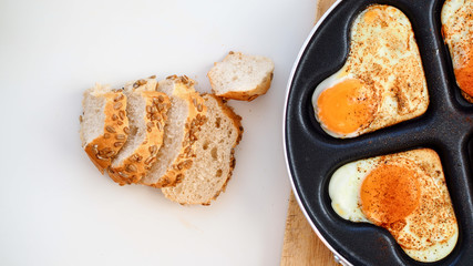 Jajka sadzone w kształcie serc na patelni leżące na drewnianej desce na białym tle