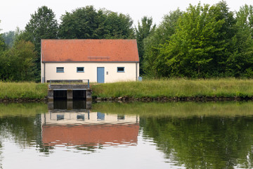 Obraz premium Pump house with red roof in the forest next to a river