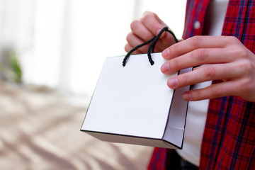 Woman in T-shirt holding a paper white gift bag at home. Making purchases for yourself and...
