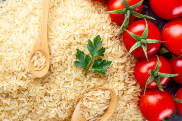 Texture of dry golden yellow long rice with wooden spoons, ripe tomatoes cherry and fresh green parsley
