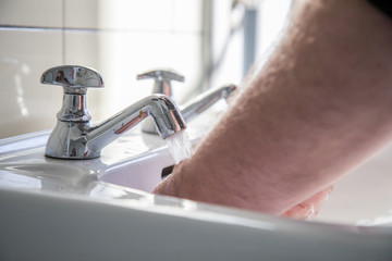 Mann nutzt Waschbecken mit Leitungswasser zum Händewaschen