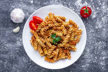 Plate of homemade pasta fusilli with meat, parsley, seasoning and ripe vegetables for lunch. Top view