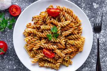 Plate of homemade pasta fusilli with meat, parsley, seasoning and ripe vegetables for lunch. Top view