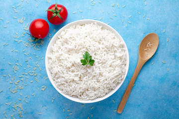 Bowl with white boiled rice with green fresh parsley and ripe tomatoes cherry for delicious healthy lunch on a blue background. Cereal food and dishes. Top view