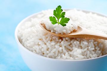 Bowl with boiled rice with green fresh parsley for delicious healthy lunch on a blue background close up. Cereal food and dishes.